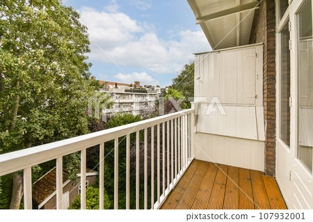 a balcony with wooden flooring and white railings on the side of a house, surrounded by lush green trees 107932001