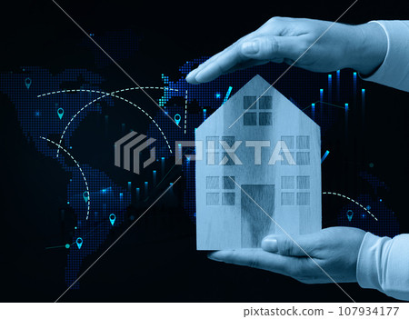 Female hands hold a wooden house against the backdrop of a world map, representing the concept of real estate purchase 107934177