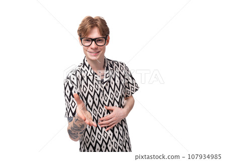 a young man with red hair in glasses and a summer black and white shirt extends his hand in greeting a young man with red hair in glasses and a summer black and white shirt extends his hand in greeting 107934985