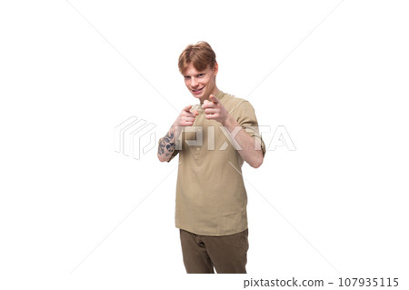 young cheerful caucasian man with red hair is dressed in a khaki shirt and brown trousers 107935115