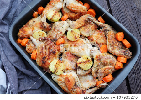 Roasted Rabbit Haunches in Pan with Stewed Vegetables on Rustic Wooden Table Surface 107935270
