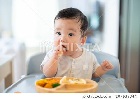 A 9-month-old baby who is in a good mood after grabbing and eating in the late stage of baby food 107935344