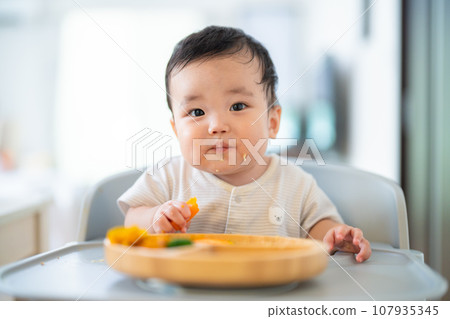 A 9-month-old baby who is in a good mood after grabbing and eating in the late stage of baby food 107935345