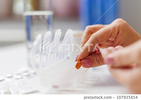 Woman hand putting pills into open pill organizer or plastic pillbox 107935854