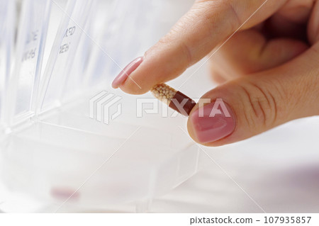 Woman hand putting pills into open pill organizer or plastic pillbox 107935857