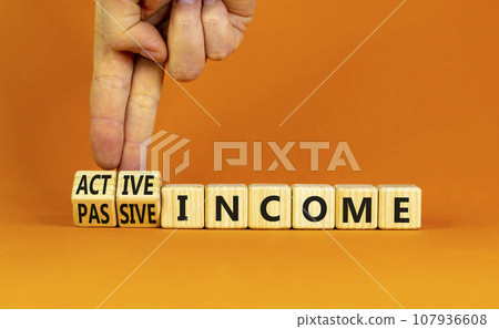 Passive or active income symbol. Businessman turns wooden cubes and changes words passive income to active income. Beautiful orange background, copy space. Business, passive or active income concept. Passive or active income symbol. Businessman turns wooden cubes and changes words passive income to active income. Beautiful orange background, copy space. Business, passive or active income concept. 107936608