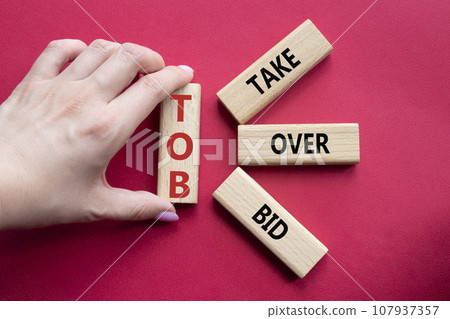 TOB - Take Over Bid. Wooden cubes with words TOB. Businessman hand. Beautiful red background. Business and TOB concept. Copy space. 107937357