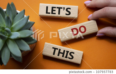 Lets do this symbol. Concept word Lets do this on wooden blocks. Businessman hand. Beautiful orange background with succulent plant. Business and Lets do this concept. Copy space 107937783