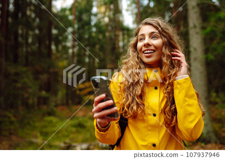 Travel apps. Curly young woman traveler in yellow coat holding smartphone in hand. Concept of travel Travel apps. Curly young woman traveler in yellow coat holding smartphone in hand. Concept of travel 107937946