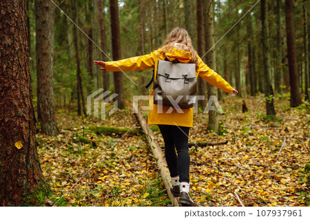 Happy tourist with backpack walking on log in forest, balancing 107937961