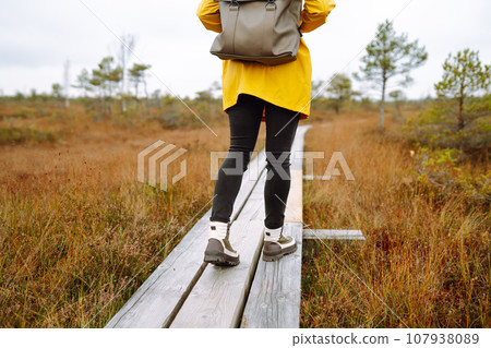 Close-up of legs in boots of woman tourist walking along wooden path against backdrop of wildlife 107938089