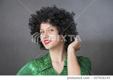 Vintage woman in afro wig and red disco costume on a gray background. Girl in the style of the seventies. 107938145