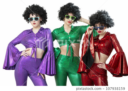 A group of disco girls in African American wigs and colorful costumes on a white background. Fashion of the seventies and eighties. 107938159