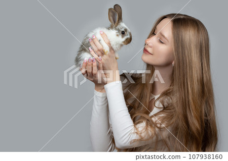 Happy young girl holding a white rabbit on a gray background 107938160