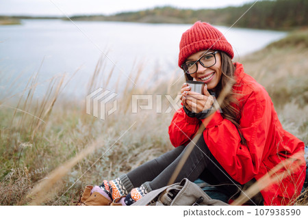 Woman holds thermos and drinks tea in autumn forest. Rest, relaxation, travel, lifestyle concept. Woman holds thermos and drinks tea in autumn forest. Rest, relaxation, travel, lifestyle concept. 107938590