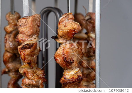 Cooking pork meat in an electric kebab maker on vertical skewers 107938642