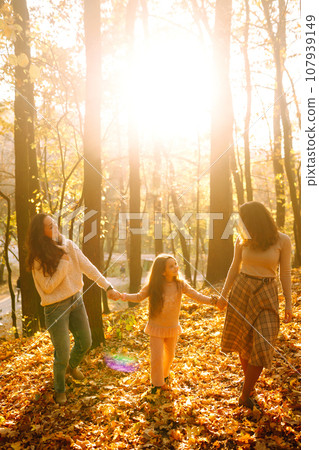 The homosexual family playing with her daughter in the autumn forest. The adventure is more fun. The homosexual family playing with her daughter in the autumn forest. The adventure is more fun. 107939149