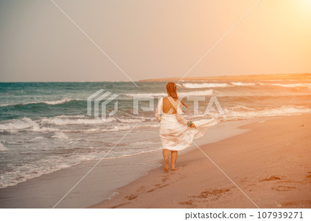 Model in boho style in a white long dress and silver jewelry on the beach. Her hair is braided, and there are many bracelets on her arms. Model in boho style in a white long dress and silver jewelry on the beach. Her hair is braided, and there are many bracelets on her arms. 107939271