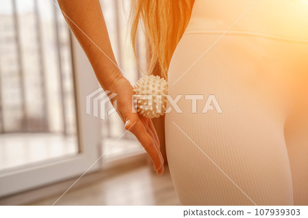 Athletic slim caucasian woman doing thigh self-massage with a massage ball indoors. Self-isolating massage 107939303