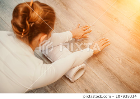 Adult athletic woman, in white bodysuit, performing fascia exercises on the floor - caucasian woman using a massage foam roller - a tool to relieve tension in the back and relieve muscle pain - the 107939334