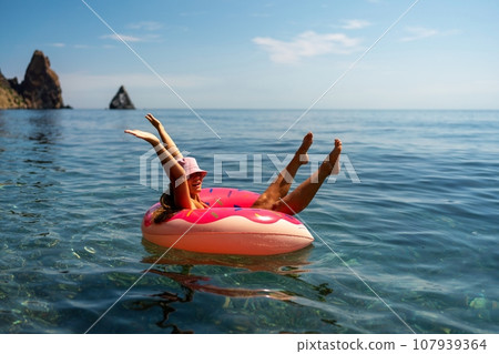 Summer vacation woman in hat floats on an inflatable donut mattress. Happy woman relaxing and enjoying family summer travel holidays travel on the sea. 107939364