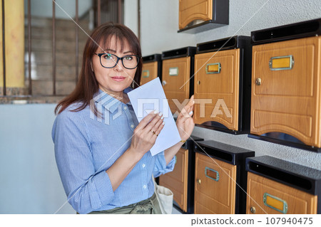 Middle-aged woman with letter near mailboxes inside an apartment building 107940475