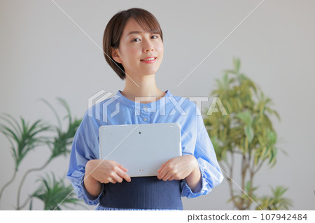 Young woman holding a tablet with both hands in front of her chest 1 Young woman holding a tablet with both hands in front of her chest 1 107942484