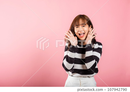 Portrait of an exuberant Asian woman making a success gesture with raised fists, expressing excitement. Studio shot isolated on pink background, radiating joy and happiness. 107942790