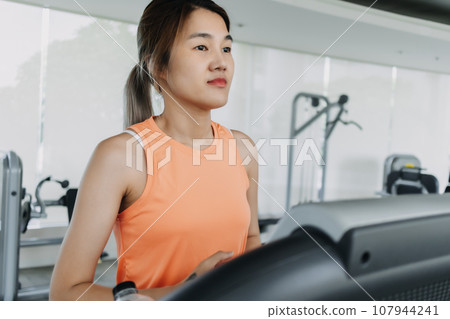 Asian woman in orange sport wears walking for exercise on treadmill in the gym Asian woman in orange sport wears walking for exercise on treadmill in the gym 107944241