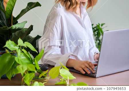 Women's hands at a laptop against a background of greenery. 107945653