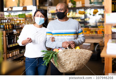 Hispanic couple in protective masks shopping in grocery store Hispanic couple in protective masks shopping in grocery store 107946208