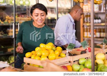 Latin american woman looking for fresh mandarines in supermarket 107946417