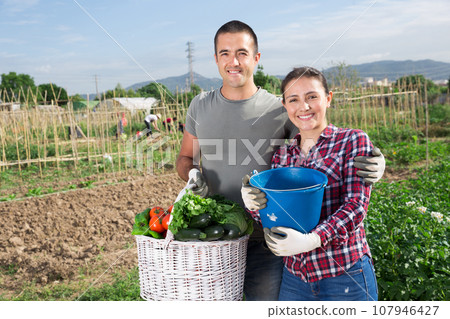 Happy couple proud of harvest of vegetables at garden 107946427
