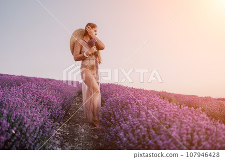 Woman lavender field. Happy carefree woman in beige dress and hat with large brim smelling a blooming lavender on sunset. Perfect for inspirational and warm concepts in travel and wanderlust. Close up 107946428