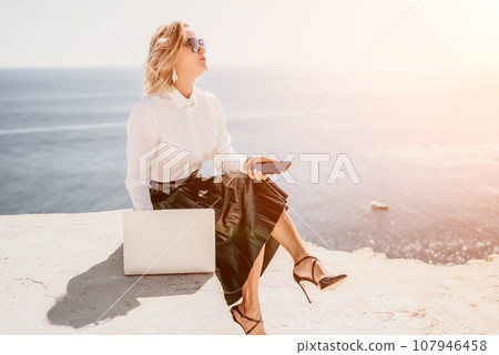 Digital nomad, Business woman working on laptop by the sea. Pretty lady typing on computer by the sea at sunset, makes a business transaction online from a distance. Freelance, remote work on vacation Digital nomad, Business woman working on laptop by the sea. Pretty lady typing on computer by the sea at sunset, makes a business transaction online from a distance. Freelance, remote work on vacation 107946458