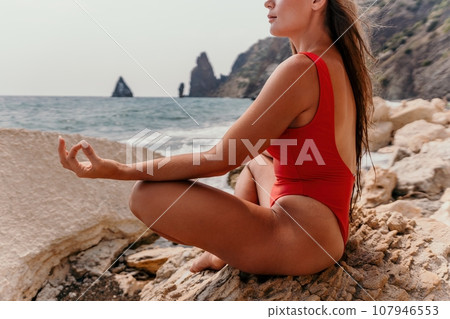 Woman sea yoga. Happy woman meditating in yoga pose on the beach, ocean and rock mountains. Motivation and inspirational fit and exercising. Healthy lifestyle outdoors in nature, fitness concept. Woman sea yoga. Happy woman meditating in yoga pose on the beach, ocean and rock mountains. Motivation and inspirational fit and exercising. Healthy lifestyle outdoors in nature, fitness concept. 107946553