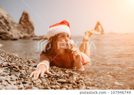 Woman travel sea. Happy tourist enjoy taking picture on the beach for memories. Woman traveler in Santa hat looks at camera on the sea bay, sharing travel adventure journey Woman travel sea. Happy tourist enjoy taking picture on the beach for memories. Woman traveler in Santa hat looks at camera on the sea bay, sharing travel adventure journey 107946749
