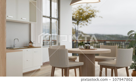 A modern Scandinavian kitchen with a dining table and a beautiful view through a balcony. A modern Scandinavian kitchen with a dining table and a beautiful view through a balcony. 107947802