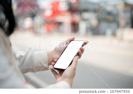Close-up image of a woman using her smartphone while walking down the street in the city. Close-up image of a woman using her smartphone while walking down the street in the city. 107947950