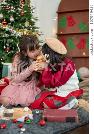 Two cute and joyful young Asian girls are enjoying eating sweets and celebrating Christmas together. 107949483