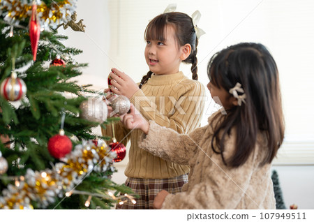 Pretty Asian girl is enjoying decorating a Christmas tree with her younger sister in the living room Pretty Asian girl is enjoying decorating a Christmas tree with her younger sister in the living room 107949511