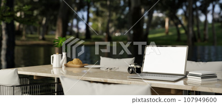 A white-screen laptop mockup on a dining table with a blurred background of a beautiful green forest A white-screen laptop mockup on a dining table with a blurred background of a beautiful green forest 107949600