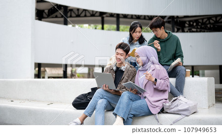 A group of diverse Asian students is working on a group project while sitting outdoors together. A group of diverse Asian students is working on a group project while sitting outdoors together. 107949653