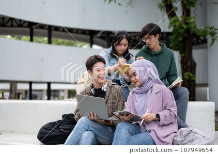 A group of diverse Asian students is working on a group project while sitting outdoors together. A group of diverse Asian students is working on a group project while sitting outdoors together. 107949654