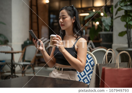 A beautiful woman is sipping coffee and using her smartphone while relaxing at a cafe or restaurant. 107949793