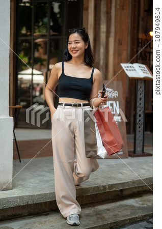 A trendy Asian woman is walking down the stairs with her shopping bags, enjoying her shopping day. 107949814