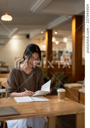 A beautiful and focused Asian woman is reading a book, doing her homework at a coffee shop. A beautiful and focused Asian woman is reading a book, doing her homework at a coffee shop. 107949904
