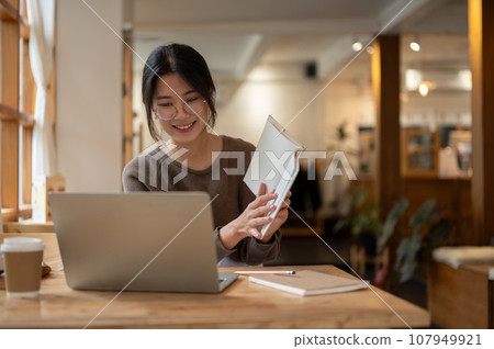 A female college student is having an online meeting or tutoring online while sitting in a cafe. 107949921