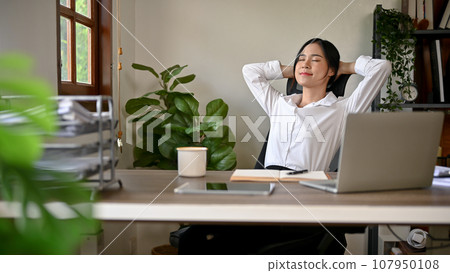 A happy and relaxed Asian businesswoman is leaning on her chair, putting hands behind her head 107950108