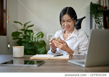 A beautiful Asian businesswoman texting with her friends on her smartphone A beautiful Asian businesswoman texting with her friends on her smartphone 107950109